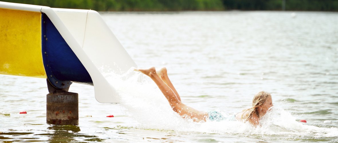 Kind rutscht auf der Wasserrutsche am Itzstedter See auf dem Bauch ins Wasser, sonniges Wetter