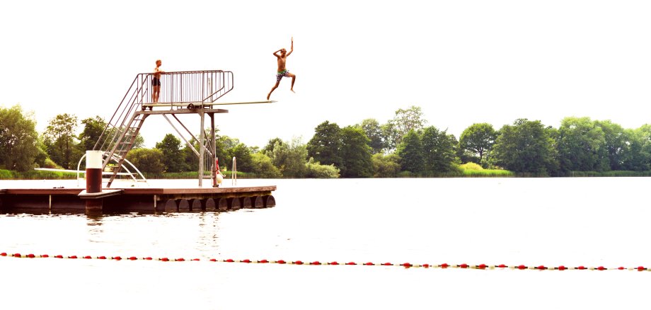 2 Jungs auf dem Sprungturm am Itzstedter See, einer springt gerade von oben ins Wasser. 